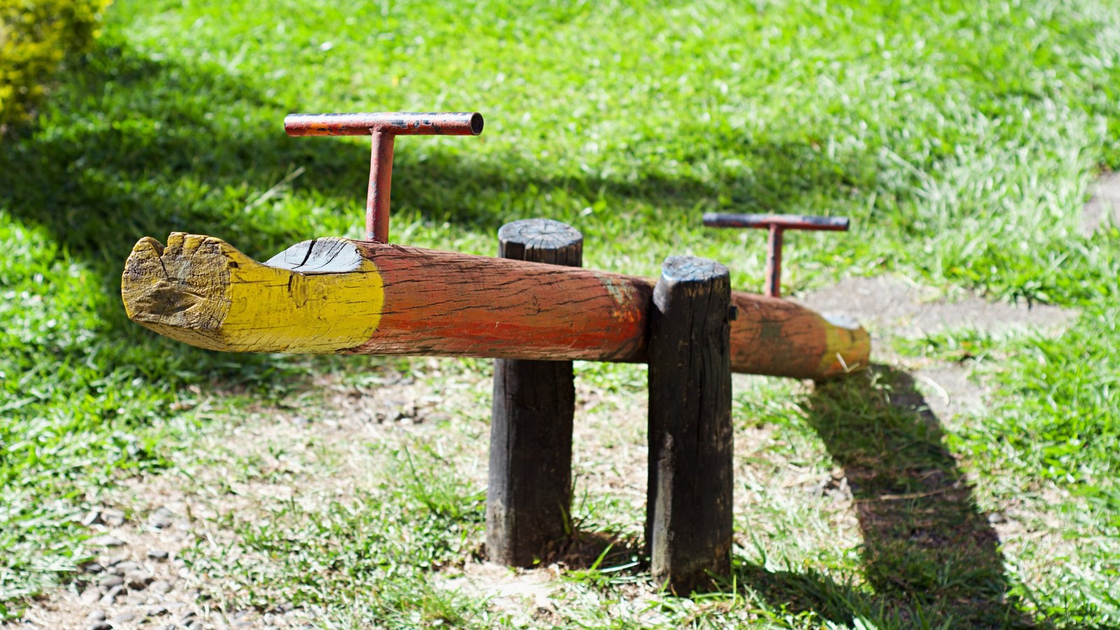 Un balancín de madera pintado en un parque, sobre la hierba al sol